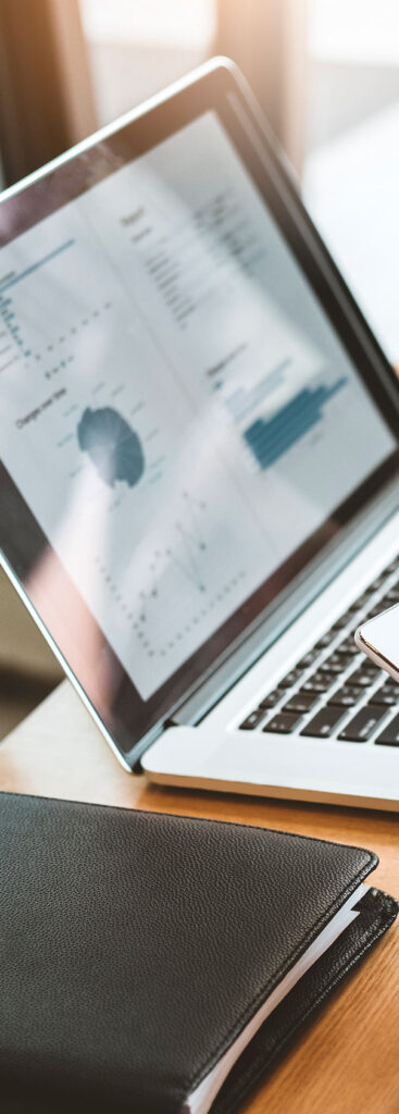 A close-up of an open laptop displaying charts and graphs on the screen, placed on a desk next to a closed black notebook.